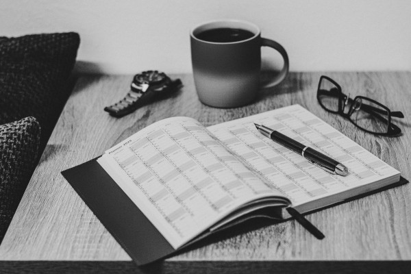 Montre, tasse, lunettes, et agenda ouvert avec un stylo plume posé dessus, le tout posé sur une table.